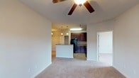 Located at 405 Grand Wailea Dr in Fayetteville, North Carolina, this single-floor residence offers a thoughtfully designed open-concept layout that seamlessly connects the living and kitchen areas. The living room features plush wall-to-wall carpeting and a ceiling fan, creating a comfortable and inviting atmosphere. A smooth transition leads into the kitchen, which is equipped with rich, dark wood cabinetry that provides ample storage space. The kitchen also features a breakfast bar peninsula with a stone-look countertop, pendant lighting overhead, and tile flooring that distinguishes it from the carpeted living areas. Black appliances, including a full-size refrigerator, complement the cabinetry for a cohesive, modern look. Neutral-toned walls throughout the space lend a clean, versatile backdrop suitable for a variety of interior styles. An additional doorway visible from the living area suggests further rooms beyond, adding to the functional flow of the home. The overall design balances practicality with comfort, making this a welcoming single-level residence in Fayetteville.