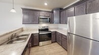 Located at 700 Town Creek Pky in Lenoir City, Tennessee, this single-floor residence offers a thoughtfully designed layout with modern finishes throughout. The kitchen is a standout feature, showcasing rich dark-stained cabinetry with detailed raised-panel doors, light granite-style countertops, and a full suite of stainless steel appliances including a refrigerator, electric range with over-the-range microwave, and dishwasher. Light wood-look flooring runs through the kitchen and adjacent areas, creating a clean, cohesive aesthetic. A peninsula with a double sink connects the kitchen to the living area, with pendant lighting adding a polished touch overhead. The living space is generously sized, finished with neutral carpet and equipped with a ceiling fan with light fixture. A glass-paned exterior door provides access to an outdoor area and allows natural light to flow into the room. The bedroom is carpeted and bright, with clean white walls and easy access to the hallway. The bathroom features a dark wood vanity with a white countertop and single sink, complemented by a wall-mounted mirror and brushed nickel fixtures, all finished with the same light wood-look flooring found throughout the unit. This residence combines practical functionality with contemporary style in a comfortable, well-organized floor plan.