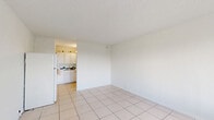 Located at 3870 N Andrews Ave in Oakland Park, Florida, this efficiently designed unit offers a functional layout across a single floor, encompassing a living room, kitchen, bathroom, and closet. The interior is finished throughout with large-format light ceramic tile flooring, which reflects natural light and contributes to a clean, airy feel.

The living area is open and simply appointed, with crisp white walls, a textured ceiling, and a wall-mounted HVAC unit. A wide sliding window and glass door open to a balcony, providing pleasant outdoor views of the surrounding tree canopy and bringing in ample natural light.

The kitchen is tucked into an alcove adjacent to the living space, featuring white cabinetry, a full-size refrigerator, and a countertop workspace. The layout makes efficient use of the available area while keeping the space organized and accessible.

The bathroom is tidy and fully equipped with a bathtub and shower combination, toilet, and vanity, all finished in white with matching tile flooring that mirrors the rest of the unit.

A louvered-door closet provides dedicated storage. The unit's consistent white palette and tile flooring throughout create a cohesive, low-maintenance living environment well-suited to the warm South Florida climate.