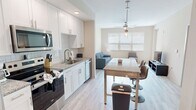 This compact yet stylish apartment maximizes its 560 square feet with a thoughtful layout and modern design. The open-concept living area combines the kitchen, dining, and living spaces, creating a sense of spaciousness. The kitchen boasts white cabinetry, stainless steel appliances, and a granite countertop with a breakfast bar, perfect for casual dining or entertaining.

The living room features a comfortable grey sofa, coffee table, and a wall-mounted TV, with large windows allowing ample natural light. The bedroom, measuring 130 square feet, includes a queen-sized bed, nightstands, and a dresser, with plush carpeting for comfort. A ceiling fan and windows provide good airflow and lighting.

The bathroom showcases a sleek design with a large walk-in shower featuring marble-look tiling, a glass door, and modern fixtures. Throughout the apartment, wood-look flooring adds warmth and durability. A spacious closet with wire shelving offers ample storage space.

Energy-efficient ceiling fans in the main living area and bedroom provide air circulation and ambient lighting. The neutral color palette and clean lines create a contemporary feel, making this apartment an ideal urban dwelling for singles or couples seeking a modern, low-maintenance lifestyle.