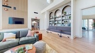 Located at 1111 Avalon Ave in San Marcos, TX, this 7,600 square foot single-story amenity center is a masterfully designed community hub combining functionality with contemporary aesthetics. The grand entrance lobby features soaring double-height ceilings, floor-to-ceiling windows that flood the space with natural light, and a striking green stone reception desk accented by curated sculptural wall art and light wood flooring. The main lounge area impresses with an expansive curtain wall of glass offering panoramic outdoor views of the pool and surrounding community, complemented by stylish sectional seating, warm-toned accent furniture, and a slatted wood media wall. A dedicated fitness center offers high vaulted ceilings, a large ceiling fan, wood-paneled accent walls, wall-mounted televisions, and a full suite of strength equipment including weight racks, cable machines, and free weights on durable tile carpet flooring. Conference and collaboration rooms feature rich burgundy walls, round wood tables, whiteboard walls, wall-mounted displays, and glazed interior windows. A cozy media lounge with leather recliner seating and vintage national park poster art provides a relaxed retreat. Throughout, light wood flooring, abundant natural light, and carefully selected artwork create a cohesive, welcoming atmosphere.