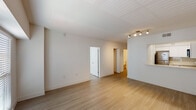 This single-floor residence offers a thoughtfully designed layout with one bedroom and one and a half bathrooms. The interior is finished with light wood-tone flooring that runs consistently throughout, creating a cohesive and airy feel across all rooms.

The open living area benefits from natural light through blinds-fitted windows and is equipped with track lighting, lending a clean, contemporary atmosphere. A pass-through detail connects the living space to the kitchen, which features white shaker-style cabinetry, white subway tile backsplash, light countertops, and a full suite of stainless steel appliances including an electric range, over-the-range microwave, and dishwasher.

The bedroom is a well-proportioned, bright room with a ceiling fan, a window with blinds, and direct access to the rest of the unit via a connecting hallway. The full bathroom includes a tiled tub-shower combination with brushed nickel fixtures, while the half bath features a vanity with white cabinetry and matching flooring. A dedicated laundry closet with louvered doors houses a stacked washer and dryer unit, adding everyday convenience. The overall palette is bright white with warm wood accents, giving the space a clean, modern character.