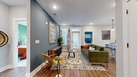 Located at 2010 N Brevard St in Charlotte's vibrant NoDa neighborhood, this single-floor residence showcases a thoughtfully designed layout with modern finishes and a cohesive, contemporary aesthetic throughout. The open living area makes a strong first impression with rich hardwood-style flooring, bold slate-blue accent walls, recessed lighting, and a door providing direct access to an outdoor area, allowing natural light to fill the space. Built-in shelving and a dedicated entryway add both function and character.

The kitchen is well-appointed with crisp white cabinetry, a classic subway tile backsplash, stainless steel appliances including a side-by-side refrigerator, and a waterfall-edge island with a built-in sink and seating — ideal for casual dining and entertaining. Pendant lighting adds a refined touch overhead.

Two bedrooms offer distinct personalities: one with a calming teal accent wall and large windows, and another featuring a sage green accent wall with ample natural light and plush carpeting. A spacious walk-in closet with wire shelving provides generous storage.

The bathroom is finished with a white vanity, quartz countertop, bold matte black fixtures, a large framed mirror, and a full tub-shower combination with clean tile surround. Every detail reflects a modern, urban sensibility.