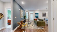 Located at 2010 N Brevard St in Charlotte's vibrant NoDa neighborhood, this single-floor residence showcases a thoughtfully designed layout with modern finishes and a cohesive, contemporary aesthetic throughout. The open living area makes a strong first impression with rich hardwood-style flooring, bold slate-blue accent walls, recessed lighting, and a door providing direct access to an outdoor area, allowing natural light to fill the space. Built-in shelving and a dedicated entryway add both function and character.

The kitchen is well-appointed with crisp white cabinetry, a classic subway tile backsplash, stainless steel appliances including a side-by-side refrigerator, and a waterfall-edge island with a built-in sink and seating — ideal for casual dining and entertaining. Pendant lighting adds a refined touch overhead.

Two bedrooms offer distinct personalities: one with a calming teal accent wall and large windows, and another featuring a sage green accent wall with ample natural light and plush carpeting. A spacious walk-in closet with wire shelving provides generous storage.

The bathroom is finished with a white vanity, quartz countertop, bold matte black fixtures, a large framed mirror, and a full tub-shower combination with clean tile surround. Every detail reflects a modern, urban sensibility.