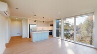 This well-designed single-floor home offers three bedrooms and two bathrooms within a thoughtfully laid-out floor plan. The open-concept kitchen serves as the heart of the home, featuring sleek light grey shaker-style cabinetry extending to the ceiling, a herringbone tile backsplash, stainless steel appliances including a gas range, built-in microwave, and French door refrigerator, and a central island with a crisp white quartz countertop. Stylish cone-shaped pendant lights hang above the island, adding a modern touch. Floor-to-ceiling windows flood the living and kitchen areas with abundant natural light while framing lush green tree views. Light hardwood flooring runs seamlessly throughout the entire space, enhancing its bright, airy feel. The spacious primary bedroom includes large sliding glass doors and a dedicated walk-in closet with dual hanging rods. Additional bedrooms are well-proportioned with ample natural light. Both bathrooms are finished in a clean, contemporary style — one features a soaking tub with grey tile surround, while the second offers a long vanity with generous counter space. A hallway connects the private spaces efficiently, and in-unit stacked laundry is conveniently accessible. The overall aesthetic is clean, modern, and move-in ready.