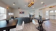 This well-appointed single-floor commercial space offers a thoughtfully designed layout that balances collaborative and private functions. The centerpiece is a spacious open-plan lounge and gathering area featuring vaulted ceilings, recessed lighting, and a striking pendant chandelier. Comfortable leather seating arrangements surround sleek coffee tables, while wall-mounted televisions and ample natural light from multiple large windows create an inviting, productive atmosphere. High-top tables and bar seating provide additional casual workspace near the lounge.

The kitchenette is equipped with stainless steel appliances, white shaker cabinetry, and dark countertops, complemented by a self-serve refreshment station. A dedicated copy and supply room features white cabinetry with subway tile backsplash and dark countertops, with a window that brings in natural light.

Private office spaces include a manager's or director's office with a full workstation and guest seating, as well as an open co-working room with individual workstations divided by partitions and large windows offering views of the surroundings. A bright, wide corridor connects all areas and leads to restrooms and a fitness room visible at the far end. Throughout the space, wood-look tile flooring and crisp white walls create a clean, cohesive, and professional aesthetic.