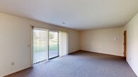 This single-floor, one-bedroom, one-bathroom unit in Grand Blanc, Michigan is designed for comfortable, efficient living. The expansive carpeted living room is a standout feature, bathed in natural light through a large sliding glass door fitted with vertical blinds that opens to a view of lush green outdoor grounds, creating a bright and welcoming atmosphere. Adjacent to the living room, the dining area features light tile flooring, a charming gold chandelier, and a latticed window with vertical blinds that continues the theme of natural light throughout the home. The combined dining and kitchen space is well-equipped with white cabinetry featuring wood-trim accents, black appliances including a range, dishwasher, and refrigerator, and ample counter space with a double sink — all set on clean light tile flooring. The generously sized bedroom offers plush carpeting, a large closet with bifold doors providing substantial storage, and a window that fills the room with natural light. The full bathroom includes tile flooring, a tub/shower combination with grab bars, and a vanity. Additional practical spaces include a pantry, utility room, hallway, and two closets, rounding out this well-organized and functional home.