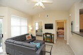 This single-floor residence offers a thoughtfully designed layout with comfortable living spaces and practical features throughout. The open living and dining area serves as the heart of the home, with warm yellow-toned walls, plush carpeting, and an abundance of natural light streaming through large windows fitted with blinds. A sliding glass door leads to a private balcony, extending the living space outdoors. The living room accommodates a generous sectional sofa and a compact dining set with bold red chairs, creating a welcoming atmosphere for both relaxing and entertaining. The kitchen is functionally equipped with light wood cabinetry, dark countertops, tile flooring, and a full suite of black appliances including a refrigerator, range, and built-in microwave. The primary bedroom features soft carpet, angled ceilings, and matching wood furniture, offering a calm and restful retreat. A second bedroom benefits from dual windows that fill the room with natural light and includes a charming window seat, while a third bedroom provides a cozy, versatile space with ample wall space for decor. The shared bathroom includes a vanity with dark countertop, a large mirror, and tile flooring, connecting conveniently to the surrounding bedrooms. Neutral tones and consistent finishes tie the entire space together cohesively.
