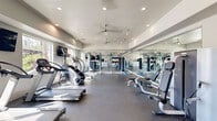 Located in Peoria, Arizona, this fitness center at 8092 W Paradise Ln offers a comprehensively outfitted workout space designed to support a full range of exercise disciplines. The single-floor facility features a clean, modern aesthetic with crisp white walls, recessed lighting, and dual ceiling fans that ensure a comfortable environment during workouts.

The cardio section is well-appointed with multiple Cybex treadmills, a StairMaster, and elliptical machines, all arranged along the windowed perimeter to allow natural light to fill the space. Flat-screen televisions are mounted on the walls for entertainment during cardio sessions.

The strength and functional training area includes a RAX multi-functional training rig with suspension straps, medicine balls, and a punching bag for combat-style conditioning. A dedicated strength zone houses selectorized cable and resistance machines, adjustable benches, and free weight storage, catering to both beginner and advanced users.

Floor-to-ceiling mirrors line one full wall, visually expanding the space and allowing users to monitor their form throughout their workout. The durable rubber flooring throughout provides safety and stability across all exercise zones.

The facility's open, rectangular layout ensures efficient use of the available floor area while maintaining ample clearance between equipment stations. With its modern design, diverse equipment selection, and well-lit atmosphere, this fitness center delivers a professional-grade workout experience.