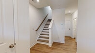 This three-story home offers a well-organized layout across its floors, with light hardwood flooring and a crisp white interior palette maintained consistently throughout. The entry level features a welcoming foyer with a staircase finished in warm wood treads and white risers with a wood handrail, providing an immediately clean and modern first impression.

The main living floor hosts an open-concept kitchen and living area flooded with natural light from multiple windows. The kitchen is equipped with white shaker-style cabinetry, granite countertops, a tile backsplash, stainless steel appliances including a side-by-side refrigerator, and a central island with pendant lighting overhead. A door provides direct outdoor access from this level.

The upper floors accommodate four bedrooms, including a generously sized primary bedroom featuring a ceiling fan, natural light from dual windows, and direct access to a private bathroom. Additional bedrooms are well-proportioned with closets and access to hallway bathrooms. All four bathrooms maintain a uniform clean design with white vanities, wood-toned flooring, and shower-tub combinations. Two hallways connect the bedrooms across the upper floors, ensuring efficient circulation throughout the home.