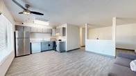 Located at 1469 Zepol Rd in Santa Fe, NM, this one-bedroom, two-bathroom unit offers a thoughtfully arranged single-floor layout that maximizes every square foot. The open-concept living and kitchen area forms the heart of the space, where light gray laminate flooring runs seamlessly throughout, complemented by white walls and a textured ceiling. The living area features a ceiling fan, a wall-mounted AC unit, and a large window that invites natural light and outdoor views, creating a bright and airy atmosphere. A half-wall partition neatly separates the living space from the kitchen zone, adding architectural definition without closing off the open feel. The kitchen is well-equipped with gray flat-front cabinetry, white countertops, a stainless steel refrigerator, a dishwasher, and a range, all arranged in an efficient L-shaped configuration with a skylight above for added brightness. The bedroom is a generously proportioned room featuring a baseboard heater and ample space, while a dedicated closet provides practical storage. Two bathrooms serve the unit conveniently. Throughout the space, the clean, neutral palette and consistent flooring create a cohesive and functional living environment well-suited to Santa Fe's practical residential character.