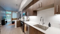 Located at 17371 NE 67th Ct in Redmond, WA, this thoughtfully designed one-bedroom, one-bathroom residence maximizes every inch of its compact footprint with modern finishes and a cohesive, contemporary aesthetic throughout. Light-toned hardwood-style flooring flows seamlessly across the entire space, lending a clean and unified feel.

The galley-style kitchen is a standout, featuring rich dark wood cabinetry that extends to the ceiling, crisp white quartz countertops, a white subway tile backsplash, stainless steel appliances, and a deep undermount sink with a chrome pull-down faucet. Under-cabinet lighting and a sleek pendant light add warm, functional illumination. A peninsula counter with bar seating doubles as a casual dining area.

The living room is anchored by a bold botanical-patterned accent wall and large floor-to-ceiling windows with direct access to an outdoor patio, flooding the space with natural light and views of the surrounding greenery. The bedroom continues the bold design language with a dramatic abstract-print accent wall, a large window with outdoor views, and comfortable carpeted flooring. A dedicated closet provides practical storage.

The bathroom is finished with large-format tile in the shower-tub surround, a quartz vanity, and wood-toned cabinetry, maintaining the modern palette found throughout the home.
