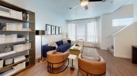 This two-floor residence offers a bright, contemporary layout designed for comfortable everyday living. The kitchen serves as a functional centerpiece, featuring white shaker cabinetry extending to the ceiling, granite countertops, a subway tile backsplash, stainless steel appliances, and a large island with bar seating — all set atop warm hardwood-style flooring. A convenient half bath on the main level includes a pedestal sink and hardwood-style floors, ideal for guests. The living room is generously proportioned, filled with natural light from oversized windows dressed with patterned drapes, and finished with hardwood-style flooring and a ceiling fan overhead. The primary bedroom is a serene retreat with plush carpeting, multiple windows, a ceiling fan, and direct access to an en-suite bathroom featuring white cabinetry and granite countertops. A second bedroom offers bright, airy proportions with large windows, soft carpet, and closet access. The full bathroom is finished in clean white tones, complete with a soaking tub, built-in shelving, and a shower curtain enclosure. Throughout the residence, a neutral palette, consistent finishes, and an abundance of natural light create a cohesive and inviting atmosphere across both levels.