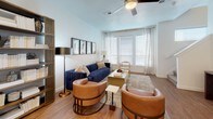 This two-floor residence offers a bright, contemporary layout designed for comfortable everyday living. The kitchen serves as a functional centerpiece, featuring white shaker cabinetry extending to the ceiling, granite countertops, a subway tile backsplash, stainless steel appliances, and a large island with bar seating — all set atop warm hardwood-style flooring. A convenient half bath on the main level includes a pedestal sink and hardwood-style floors, ideal for guests. The living room is generously proportioned, filled with natural light from oversized windows dressed with patterned drapes, and finished with hardwood-style flooring and a ceiling fan overhead. The primary bedroom is a serene retreat with plush carpeting, multiple windows, a ceiling fan, and direct access to an en-suite bathroom featuring white cabinetry and granite countertops. A second bedroom offers bright, airy proportions with large windows, soft carpet, and closet access. The full bathroom is finished in clean white tones, complete with a soaking tub, built-in shelving, and a shower curtain enclosure. Throughout the residence, a neutral palette, consistent finishes, and an abundance of natural light create a cohesive and inviting atmosphere across both levels.