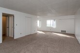 This single-floor unit is designed with a straightforward, functional layout that maximizes usable living space. The main living area is generously sized, featuring wall-to-wall beige carpeting and white walls throughout, creating a bright and neutral atmosphere. A textured popcorn ceiling adds a classic touch, while floor-level heating vents ensure year-round comfort. A large window allows natural light to fill the space, enhancing its open feel. Multiple closet doors provide ample built-in storage directly off the living area.

The kitchen is efficiently arranged with white cabinetry extending to the ceiling, offering substantial storage. It is equipped with a coil-burner electric range and oven, an under-cabinet range hood, and a double-basin stainless steel sink. Light-toned countertops and tile flooring complete the practical design.

The bathroom features a dedicated vanity area with a marble-patterned countertop, under-sink cabinet storage, and a well-lit mirror with a built-in light bar. The toilet and tiled shower/tub area are positioned in an adjoining section, offering a degree of privacy between the grooming and bathing areas. Overall, the unit presents a clean, move-in ready environment with a consistent neutral palette throughout.