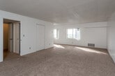 This single-floor unit is designed with a straightforward, functional layout that maximizes usable living space. The main living area is generously sized, featuring wall-to-wall beige carpeting and white walls throughout, creating a bright and neutral atmosphere. A textured popcorn ceiling adds a classic touch, while floor-level heating vents ensure year-round comfort. A large window allows natural light to fill the space, enhancing its open feel. Multiple closet doors provide ample built-in storage directly off the living area.

The kitchen is efficiently arranged with white cabinetry extending to the ceiling, offering substantial storage. It is equipped with a coil-burner electric range and oven, an under-cabinet range hood, and a double-basin stainless steel sink. Light-toned countertops and tile flooring complete the practical design.

The bathroom features a dedicated vanity area with a marble-patterned countertop, under-sink cabinet storage, and a well-lit mirror with a built-in light bar. The toilet and tiled shower/tub area are positioned in an adjoining section, offering a degree of privacy between the grooming and bathing areas. Overall, the unit presents a clean, move-in ready environment with a consistent neutral palette throughout.