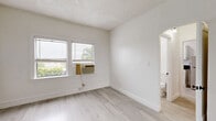 Located at 1310 S Wilton Pl in Los Angeles, CA, this single-floor 2-bedroom, 1-bathroom unit offers a clean, efficiently designed layout with a consistent bright and airy aesthetic. Light wood-style flooring runs throughout the space, complemented by white walls and white baseboards that contribute to a fresh, neutral palette.

The primary bedroom is a well-proportioned room featuring a window-mounted air conditioning unit and a window that invites natural light and outdoor views of surrounding greenery. The second bedroom is similarly bright, with large windows offering views of palm tree-lined streets — a quintessential Los Angeles backdrop — and includes a mirrored sliding closet door for added depth. Both bedrooms benefit from the unit's three closets, providing notable storage throughout.

The kitchen is efficiently arranged with white cabinetry, dark countertops, stainless steel appliances including a gas range and full-size refrigerator, and a double sink beneath a natural-light-admitting window. The layout supports practical day-to-day functionality.

The bathroom presents a clean, updated design featuring a full soaking tub with a rain-style showerhead, a dark-stained vanity with a white basin, a medicine cabinet mirror, and a window for ventilation and natural light. The textured ceilings in select rooms add a classic touch to the overall interior character.