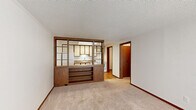 Located at 201 E Edgewood Blvd in Lansing, Michigan, this one-bedroom, one-bathroom unit offers a practical and well-organized layout across a single floor. The living room greets you at the entry, featuring plush carpeting, vertical blinds over a large window that invites natural light, and a built-in wood-trimmed room divider with open shelving that creates a stylish visual separation between the living and kitchen areas. The kitchen is equipped with white cabinetry accented by warm wood trim, laminate stone countertops, a full-size refrigerator, dishwasher, and a sink — all set atop easy-care hardwood-style flooring. The bedroom offers comfortable carpeting, a generous window with vertical blinds, and a built-in closet with a full-width hanging rod. The full bathroom includes a combined tub and shower, vanity with marble-style countertop, and hardwood-style flooring. A dedicated laundry room houses a full-size washer and dryer alongside a water heater, adding everyday convenience. A hallway connects all rooms efficiently, completing this thoughtfully arranged space ideal for comfortable single-occupant living.