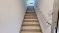 This three-story townhome offers a thoughtfully designed layout that maximizes functionality across each level. The ground floor features a private garage with a concrete floor, built-in water heater storage beneath the staircase, and direct interior access — providing both secure parking and practical utility space.

The main living level presents an open-concept kitchen and living room anchored by rich hardwood flooring that transitions to warm stone-tiled flooring in the kitchen. The kitchen is well-equipped with stainless steel appliances, including a French door refrigerator, range, microwave, and dishwasher, complemented by white shaker-style cabinetry, a tile backsplash, and a central island with a clean white countertop. Recessed lighting illuminates the space, and large windows allow natural light to flow into the living area.

The upper floor hosts the spacious primary bedroom, featuring plush carpeting, crown molding with gray trim accents, a ceiling fan, and French doors that open to an outdoor balcony. Two closets and three full bathrooms — one featuring a soaking tub with white tile surround — provide ample storage and convenience. A dedicated laundry area and carpeted staircases with handrails connect the levels seamlessly, rounding out this well-structured and comfortable multi-level home.