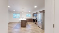Located in Rathdrum, Idaho, this well-appointed 2-bedroom, 2-bathroom unit offers a thoughtfully designed single-level layout. The open-concept kitchen and living area serves as the heart of the home, showcasing rich dark-brown cabinetry, a central island with a built-in sink and pendant lighting, white quartz countertops, a subway tile backsplash, and a full suite of stainless steel appliances including a refrigerator, range, and dishwasher. Light-toned luxury vinyl plank flooring runs throughout, creating a warm and cohesive aesthetic. The living area is bright and airy, benefiting from multiple windows with views of the surrounding landscape and a glass-panel door that invites natural light. Both bedrooms are generously proportioned, with the primary bedroom featuring large windows and outdoor access, while the secondary bedroom includes a sliding closet and a wall-mounted mini-split HVAC unit for individualized climate control. The bathrooms are finished with large-format tile flooring, white cabinetry, and clean, modern fixtures. A dedicated laundry room houses a full-size front-loading washer and dryer alongside the water heater. Two closets provide ample storage throughout the unit.