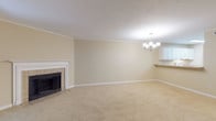 This single-floor residence offers a practical and cohesive layout with neutral warm-beige walls, white trim, and plush carpet throughout the main living and bedroom areas. The spacious living room serves as the centerpiece of the home, highlighted by a classic white-mantled fireplace with tile surround and an elegant multi-light chandelier overhead. Crown molding adds a refined architectural detail along the ceiling perimeter. Adjacent to the living area, the dining space benefits from a sliding glass door that introduces natural light and provides views of surrounding greenery, further illuminated by a matching chandelier.

The kitchen is efficiently arranged with ample white cabinetry, light countertops, a double sink, and white appliances including a range, dishwasher, and refrigerator. Light hardwood-style flooring adds warmth to the kitchen and bathrooms.

The two bedrooms are carpeted and well-proportioned, each equipped with a ceiling fan. One bedroom includes an attached walk-in closet. Both bathrooms feature a tub-shower combination, single vanity with light countertops, white cabinetry, and hardwood-style flooring, presenting a clean and uniform aesthetic throughout the home.