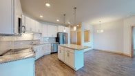 Located at 3601 Cross Hill Dr in Madison, Wisconsin, this single-floor residence offers a thoughtfully designed open-concept layout with contemporary finishes throughout. The kitchen serves as a central highlight, featuring crisp white cabinetry with brushed nickel hardware, granite countertops, a subway tile backsplash, stainless steel appliances including a refrigerator, range, microwave, and dishwasher, and a central island with pendant lighting overhead. Wood-look plank flooring runs through the kitchen and living areas, lending warmth and continuity to the space. The living area is open and airy, with access to a sliding glass door that brings in natural light. The bedroom is carpeted for comfort, includes a ceiling fan, a large window overlooking the surrounding neighborhood, and a dedicated walk-in closet with built-in shelving. The bathroom is well-equipped with granite countertops, a wide vanity with an undermount sink, a full soaking tub with shower, and wood-look flooring that ties the space together. A second bathroom provides additional convenience with a similar granite vanity and clean, modern finishes. The overall design balances functionality with contemporary style throughout.