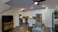This two-floor space showcases a thoughtfully designed open-concept layout where the kitchen and living area flow seamlessly together. The kitchen is outfitted with a full suite of stainless steel appliances, including a French door refrigerator, electric range with microwave above, and dishwasher. Crisp white shaker-style cabinetry extends to the ceiling, offering generous storage, while a tile backsplash adds a subtle textural detail. The countertops complement the clean, contemporary aesthetic, and the undermount sink is positioned beneath upper cabinets for practical workspace.

Dark hardwood flooring runs throughout, creating a rich contrast against the white kitchen elements and light-toned walls. Recessed lighting provides consistent illumination across the open area, while a ceiling fan with an integrated light fixture serves as a functional focal point overhead. The living area transitions naturally from the kitchen, accommodating comfortable seating and a casual coffee table arrangement. The overall ambiance is modern and well-appointed, with a neutral palette that creates a bright, welcoming atmosphere across both levels.