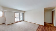 This single-floor unit offers a practical and well-organized layout designed for comfortable everyday living. The living area greets you with neutral tones, plush carpeting, and a sliding glass door that fills the space with natural light and provides access to an outdoor balcony with views of the surrounding landscape. The open flow connects seamlessly to a dining area, which features warm hardwood-style flooring and a ceiling fan overhead, creating a cohesive and inviting atmosphere.

The kitchen is efficiently designed with a galley-style configuration, offering ample wooden cabinetry, light-toned countertops, and black appliances including a refrigerator, range, and dishwasher. Hardwood-style flooring continues through this space, complementing the warm wood cabinetry tones.

Two well-sized bedrooms are finished with soft carpeting and natural light provided by individual windows. The primary bedroom includes a walk-in closet with open shelving and direct access to the full bathroom. The bathroom is neatly appointed with a single-sink vanity featuring wooden cabinetry, a tub-shower combination, and tile flooring.

Throughout the unit, consistent warm wood trim, neutral wall tones, and a clean, understated design create a cohesive and functional living environment.