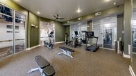 Located at 300 Seven Springs Way in Brentwood/Nashville, TN, this fitness center offers a comprehensive, single-level exercise room designed to support a full range of workout routines. The space features olive-green accent walls, recessed lighting, and durable rubber-composite flooring throughout, creating a clean and functional training environment. Ceiling fans are positioned throughout to ensure comfortable airflow during workouts.

The cardio zone is well-appointed with multiple treadmills and elliptical trainers, while the strength training area includes a multi-functional cable machine, a full dumbbell rack ranging across multiple weight increments, and several adjustable weight benches. A large wall-mounted mirror spans one side of the room, amplifying the sense of space and allowing users to monitor their form. A flat-screen TV is mounted above the mirror for entertainment during workouts.

Floor-to-ceiling glass partition walls separate an adjacent studio space, which is visible from the main floor and adds an open, modern aesthetic. Large windows along the exterior walls invite natural light and provide views of the surrounding outdoor area. The thoughtful layout ensures ample circulation space between equipment, making the fitness center accessible and practical for users of all fitness levels.