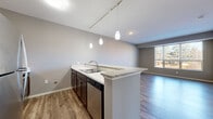 Located at 1428 W Arrowhead Rd in Duluth, MN, this well-appointed one-bedroom, one-bathroom unit offers a thoughtfully designed layout across a single floor. The open-concept kitchen and living area serves as the heart of the space, anchored by a peninsula with granite countertops that doubles as a breakfast bar. Rich dark cabinetry pairs with stainless steel appliances — including a refrigerator, range, and microwave — while elegant pendant lighting suspended from a track system adds a modern, refined touch. Hardwood-style flooring runs throughout the main living areas, complementing the neutral gray walls and creating a cohesive, contemporary aesthetic. A large window in the living area invites abundant natural light and offers views of the surrounding wooded landscape. The bedroom is a comfortable retreat featuring plush carpeting, a closet, and a bright window overlooking the tree-lined exterior. The full bathroom is well-finished with a dark wood vanity, white countertop, a tub-shower combination, and wood-look flooring that ties together the overall design palette. A hallway connects all areas efficiently, completing this clean and functional single-floor layout ideal for comfortable everyday living in Duluth.