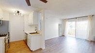 This well-designed 1-bedroom, 1-bathroom unit offers a clean, modern aesthetic across a single floor. The open-concept layout seamlessly connects the kitchen and living room, creating a functional and airy feel. The kitchen features white cabinetry with matte black hardware, stainless steel appliances including a gas range, microwave, refrigerator, and dishwasher, along with a gold-toned sink and a dedicated pantry area. Light hardwood flooring runs throughout the unit, complementing the crisp white walls and textured ceilings. A ceiling fan with a wood accent adds a touch of warmth to the living area, which is bathed in natural light from a large sliding glass door that opens to a private balcony. A wall-mounted HVAC unit provides climate control in the living space. The bedroom is a comfortable size, featuring a mirrored sliding closet door, a window with sheer curtains, and direct access to the full bathroom. The bathroom is outfitted with a modern vessel-style sink, a mirrored medicine cabinet with ample storage, a wall-mounted towel ring, and clean, minimalist finishes throughout. The unit's bright, neutral palette and updated fixtures create a cohesive and inviting living environment.