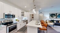This 2-bedroom, 2-bathroom residence is designed with a clean, contemporary aesthetic and a functional open floor plan. The combined kitchen and living area forms the heart of the home, featuring a chef-inspired kitchen outfitted with white shaker cabinetry, subway tile backsplash, stainless steel appliances, and a large center island with pendant lighting — ideal for both meal preparation and casual dining. The adjacent living room is bright and inviting, with wood-look flooring, a ceiling fan, and sliding glass doors that open to a private balcony with outdoor views. Both bedrooms are generously proportioned, with the primary bedroom offering ample closet space and direct access to a well-appointed en-suite bathroom featuring a wide white vanity, modern fixtures, and a walk-in shower. The second bedroom is equally comfortable, benefiting from multiple windows that draw in natural light. The second bathroom mirrors the same crisp, bright design. Additional highlights include a dedicated laundry area with a full-size washer and dryer, two closets for extra storage, and a welcoming entrance. Throughout the home, a consistent palette of white walls and wood-tone flooring creates a cohesive, modern ambiance.
