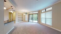 This single-floor residence offers a thoughtfully designed layout with a seamless flow between living, dining, and kitchen areas. The spacious living room is a standout feature, highlighted by large sliding glass doors that open to a private balcony overlooking lush greenery, flooding the space with natural light. Transom windows above further enhance the bright, airy atmosphere, while plush carpeting, crown molding, and built-in shelving add warmth and character.

The open-concept kitchen connects directly to the living and dining areas via a breakfast bar with dark granite countertops. Rich dark wood cabinetry, stainless steel appliances including a gas range and microwave, and light tile flooring complete a functional and stylish culinary space. Pendant lighting above the bar adds a refined touch.

The bedrooms are generously sized, each featuring soft carpeting, crown molding, and windows fitted with blinds for privacy and light control. One bedroom includes a ceiling fan for added comfort.

Two full bathrooms are finished with light tile flooring, dark wood vanities, and white countertops. The primary bath includes a glass-enclosed walk-in shower with decorative tile accents, while the secondary bath offers a full tub-shower combination with matching tilework. Both bathrooms are clean, practical, and well-appointed.