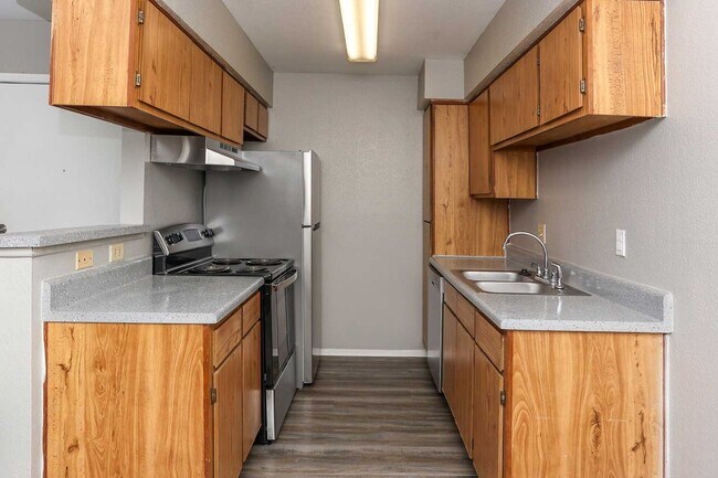 Cocina tipo galera con gabinetes de madera, encimeras grises, fregadero doble, estufa eléctrica y refrigerador de tamaño completo. - Park at Summerhill