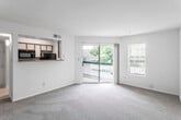 This single-floor residence offers a bright, open layout designed for comfortable everyday living. The spacious living room serves as the heart of the unit, featuring neutral wall-to-wall carpeting and an abundance of natural light drawn in through a large sliding glass door that opens onto a private balcony with outdoor views of surrounding greenery. A secondary window further enhances the airy feel of the space.

The kitchen is accessible via a pass-through counter that overlooks the living area, creating a connected, open feel between the two spaces. The galley-style kitchen is equipped with black appliances—including a refrigerator, range, microwave, and dishwasher—alongside warm wood-toned cabinetry, light countertops, and tile flooring. A narrow window above the sink provides additional natural light.

The bedrooms are carpeted and well-proportioned, each featuring neutral tones and windows that bring in natural light and outdoor views. The rooms offer a clean, versatile canvas suitable for a variety of furniture arrangements.

The bathroom includes a single-sink vanity with wood cabinetry and a large mirror, paired with a full tub and shower combination. Tile flooring completes the practical, functional design of the space.