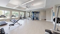 Located at 1307 Ridge Rd in Rockwall, Texas, this single-floor fitness center is thoughtfully designed to accommodate a wide range of workout styles and fitness goals. The space is divided into several distinct functional zones, each appointed with quality equipment and a clean, modern aesthetic characterized by neutral gray tones, light-toned flooring, and crisp white trim.

The cardio area houses a row of treadmills, elliptical trainers, and a rowing machine positioned alongside large windows that invite natural light and outdoor views. Full-length mirrors line the walls, enhancing the sense of openness throughout. A dedicated strength training zone features a multi-station cable machine, a weight bench, and a comprehensive dumbbell rack spanning a wide range of weights, complemented by stability balls for functional training.

A separate cycling studio provides a focused environment for spin workouts, equipped with multiple stationary bikes with digital displays and anchored by a floor-to-ceiling mirror wall. Oversized ceiling fans and recessed linear lighting ensure comfort during high-intensity sessions.

An adjoining open studio area with exercise mats offers ample space for yoga, stretching, or group fitness classes. Tray ceilings add architectural distinction, while large ceiling fans maintain airflow. Together, these zones create a comprehensive, well-organized facility suited for diverse fitness routines.