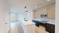 This well-appointed 2-bedroom, 3-bathroom single-floor residence offers a thoughtfully designed open-concept layout with modern finishes throughout. The kitchen serves as a central hub, featuring a large waterfall island with an undermount sink, two-tone cabinetry with light wood uppers and dark navy lowers, stainless steel appliances, and a geometric tile backsplash. Pendant lighting anchors the space, which flows seamlessly into the living area. Light wood-look flooring runs throughout, complementing the clean white walls and recessed lighting. The spacious primary bedroom includes a ceiling fan, large windows that draw in abundant natural light, and direct access to a well-organized walk-in closet with built-in shelving and hanging rods. The en-suite bathroom is finished in crisp white tile and features a stand-up shower with black-framed glass doors, a floating dark vanity, and matte black fixtures. A second full bathroom mirrors this modern aesthetic with a tiled tub-shower combination and matching hardware. The second bedroom is bright and well-proportioned, also equipped with a ceiling fan. A private balcony with metal railing offers views of a communal courtyard below, providing an inviting outdoor retreat.