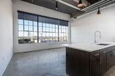 Located at 1143 First Ave S in Birmingham, Alabama, this single-floor unit showcases an industrial-modern aesthetic that blends raw architectural character with contemporary finishes. The space retains its industrial roots through exposed ductwork, structural timber beams, and polished concrete floors that extend throughout the open layout, creating a cohesive and stylish foundation.

The main living area is anchored by a large, multi-pane factory-style window that floods the space with natural light and offers sweeping views of the surrounding Birmingham cityscape. The kitchen is a standout feature, centered around a substantial island with an integrated sink and modern pendant lighting overhead. White upper cabinetry, a subway tile backsplash, stainless steel appliances—including a refrigerator, range, and built-in microwave—complete the well-appointed cooking space. A stacked washer and dryer unit is conveniently integrated nearby.

Private rooms offer quieter retreats, with neutral walls, concrete or carpeted floors, and original structural columns adding character. The bathroom is cleanly finished with white subway tile in the glass-enclosed shower, a white vanity, and polished concrete flooring, maintaining the unit's consistent industrial-modern design language throughout.