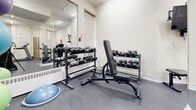 Located at 890 Mount Pleasant in Toronto's vibrant Davisville Village neighbourhood, this fitness room offers a well-equipped exercise space designed to support a variety of workout routines. The room features durable rubber flooring throughout, providing a safe and practical surface for both cardio and strength training activities. Bright flush-mount fluorescent lighting illuminates the space evenly, contributing to a clean and functional atmosphere.

Cardio equipment includes a Landice treadmill and an Octane elliptical trainer, both positioned to allow comfortable use. A stationary recumbent bike rounds out the cardio offerings. For strength training, the room is furnished with a multi-tier dumbbell rack stocked with a comprehensive range of free weights, accompanied by an adjustable workout bench. Stability and balance tools, including exercise balls and a BOSU ball, add versatility to available workout options.

A large wall-mounted mirror spans one side of the room, enhancing the sense of space while allowing users to monitor their form during exercise. A wall-mounted television provides entertainment during workouts, and a built-in water fountain ensures convenient hydration. Exercise instruction charts are posted on the walls for reference. The room is accessed through a glazed door, and a window allows a measure of natural light to filter in.