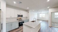 Located at 375 Greenbriar Rd in Fate, TX, this single-story residence offers a thoughtfully designed layout encompassing one bedroom, two bathrooms, and a dedicated closet. The open-concept kitchen serves as the centerpiece of the home, showcasing a large granite-topped island with an integrated sink, two-tone shaker cabinetry in white and sage green, a classic subway tile backsplash, and a full suite of stainless steel appliances including a French door refrigerator, electric range, and built-in microwave. A washer and dryer are also conveniently housed within the unit. Rich wood-look flooring flows throughout the kitchen and living areas, while the living room benefits from natural light through a window fitted with blinds and a ceiling fan overhead. The bedroom is carpeted for comfort, featuring its own ceiling fan, a window with an exterior view, and access to a well-appointed bathroom. The bathroom includes a soaking tub and shower combo with full white subway tile surround, wood-look flooring, and direct access to a walk-in closet with multi-tier hanging storage. Clean white walls and recessed lighting throughout contribute to a bright, modern aesthetic.