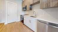 Located at 290 Revolution Dr in Somerville, MA, this single-floor unit offers a thoughtfully designed living space with a clean, contemporary aesthetic throughout. Light wood-tone flooring runs seamlessly across every room, creating a warm and cohesive foundation that complements the bright white walls and modern trim work.

The kitchen is a standout feature, showcasing a well-appointed layout with a combination of crisp white lower cabinetry and warm wood-toned upper cabinets. Stainless steel appliances — including a range, over-the-range microwave, and dishwasher — are paired with white quartz countertops and a stylish herringbone tile backsplash. A stainless steel undermount sink with a sleek pull-down faucet completes the space, offering both function and visual appeal.

The bathroom is designed with a minimalist sensibility, featuring a glass-enclosed walk-in shower with white subway tile surround and a built-in shower base. Chrome fixtures and a grab bar accent the clean lines of the space, which benefits from the same light wood flooring found throughout the unit.

The living area is open and airy, with neutral walls and a window that allows natural light to flow in. The overall design language of this unit is modern and move-in ready, with consistent finishes and attention to detail across every area.