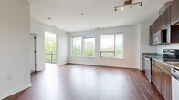 Located at 300 Riverboat Row in Newport, Kentucky, this one-bedroom, one-bathroom residence offers a well-designed layout across a single floor. The open-plan living room and kitchen area is bright and airy, featuring rich hardwood flooring, crisp white walls, and an abundance of natural light streaming through large windows that frame views of the surrounding trees and cityscape, including glimpses of a landmark bridge. A private balcony extends the living space outdoors. The kitchen is outfitted with dark walnut cabinetry, granite countertops, a textured tile backsplash, and a full suite of stainless steel appliances, including a range, microwave, dishwasher, and refrigerator. The bedroom is a comfortable retreat with plush carpeting, a ceiling fan, generous closet space, and a window overlooking the greenery and city skyline beyond. The bathroom features large-format tile flooring, a dark wood vanity, and a full soaking tub with tiled surround. A dedicated utility room rounds out the functional layout. Track lighting in the main living area and consistent finishes throughout give this residence a cohesive, modern aesthetic well-suited to urban living along the Ohio River.