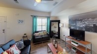 This multi-story residence is distributed across three floors and offers a practical, well-organized layout designed for comfortable everyday living. The living room serves as a central gathering space, featuring wood-style laminate flooring, a ceiling fan, and a window dressed with teal curtains that bring in natural light. The open feel is enhanced by a large floor mirror and thoughtful lighting.

The kitchen is equipped with rich cherry-toned cabinetry, dark countertops, and black appliances including a refrigerator, range, and microwave. A stacked washer and dryer unit is conveniently tucked nearby, and a dining area with a table and chairs sits adjacent to a window overlooking the exterior.

Multiple bedrooms are present throughout the unit, each featuring plush carpet flooring, generous windows with grommet-style curtains, and ample wall space. The bedrooms are well-suited for study and rest, with some including desks and shelving.

Several bathrooms are distributed across the floors, each featuring wood-style flooring, a vanity with dark wood cabinetry, and either a shower with curtain or a full shower-tub combination. The overall aesthetic is clean and functional, with a neutral color palette maintained consistently throughout the space.