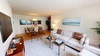 Located at 208 Milligan Rd in West Babylon, NY, this efficiently designed one-bedroom, one-bathroom residence offers a thoughtfully arranged single-floor layout. The open-concept living and dining area forms the heart of the home, showcasing warm parquet hardwood flooring throughout. The living room is bright and airy, featuring a large picture window that frames lush green outdoor views and allows abundant natural light to fill the space. The adjacent dining area is anchored by a pendant light fixture and offers comfortable space for a full dining set. The kitchen is well-equipped with rich wood cabinetry, light stone countertops, a subway tile backsplash, stainless steel appliances, and a window overlooking the greenery outside. The bedroom is a calm retreat with soft, neutral tones, sheer curtain-draped windows that invite natural light, and direct access to the hallway via hardwood flooring. The full bathroom features white tile throughout, a shower-tub combination, a mirrored medicine cabinet, and a window providing ventilation and natural light. Overall, the space presents a clean, cohesive aesthetic with a warm and comfortable ambiance throughout.