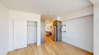Located in Portland's vibrant West End neighborhood, this efficiently designed single-floor unit at 1670 SW Alder St offers a thoughtful layout across a living room, kitchen, and bathroom. The living area is anchored by a large floor-to-ceiling window that floods the space with natural light and frames views of the surrounding Portland cityscape. Light-toned hardwood flooring runs throughout, lending warmth and visual continuity to the open layout. A closet with built-in shelving provides practical storage within the living space.

The kitchen is designed with functionality in mind, featuring a clean combination of white upper cabinetry and wood-toned lower cabinets, white quartz countertops, and a full suite of stainless steel appliances including a range with electric cooktop, over-the-range microwave, and refrigerator. A single-basin stainless steel sink and additional open wood shelving round out the kitchen's storage options.

The bathroom includes a walk-in shower with clean white surround and chrome fixtures. Throughout the unit, the design aesthetic is contemporary and minimalist, with crisp white walls, recessed lighting, and a neutral palette that maximizes the sense of space. This unit offers a practical and modern urban living experience in the heart of Portland.