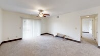 Located at 106 Castle Dr in Dothan, Alabama, this one-bedroom, two-bathroom unit offers a comfortable and functional single-floor layout. The living area features plush wall-to-wall carpeting, a ceiling fan with light fixture, and a sliding glass door framed by vertical blinds that opens to a private balcony, allowing natural light to fill the space. The kitchen is well-equipped with rich, dark wood cabinetry, granite-style countertops, a tile mosaic backsplash, hardwood-style flooring, and black appliances including an electric range and dishwasher — providing ample storage and counter space for everyday cooking. A connecting hallway with hardwood-style flooring leads to the bathrooms, one of which features a shower-tub combination with crisp white surroundings and a vanity with granite-style countertops. The generously sized primary bedroom is carpeted and includes a ceiling fan, a natural light-admitting window, and access to a dedicated walk-in closet alongside an additional louvered-door closet. Throughout the unit, neutral-toned walls, dark baseboards, and textured ceilings contribute to a clean, cohesive aesthetic. The layout flows efficiently through a central hallway connecting all rooms.