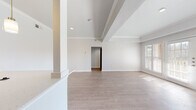 This single-floor residence offers a thoughtfully designed open layout that connects the main living areas seamlessly. The living room is a standout space, featuring a classic white-mantled fireplace framed by built-in shelving and large windows with plantation shutters that allow natural light to pour in. French doors lead to an outdoor area, adding to the bright, airy feel of the room. Crown molding and a tray ceiling add architectural refinement throughout.

The kitchen is equipped with a peninsula breakfast bar topped with light quartz countertops, pendant lighting, white cabinetry, and black appliances. An integrated sink and open sightlines to the living and dining areas make it ideal for everyday functionality.

The bedroom is generously proportioned, featuring a ceiling fan, a wide window with natural light, and direct access to a walk-in closet. Light-toned hardwood-style flooring runs consistently across all rooms, lending a cohesive and clean aesthetic.

The bathroom is well-finished, showcasing a tiled tub-shower combo with grey subway tile and a decorative mosaic border, a white vanity with quartz countertop, and warm wood-style flooring. The overall design palette—neutral whites and soft greys—creates a calm, modern atmosphere throughout this inviting space.