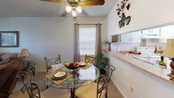 Located at 15101 Quails Bluff Cir in Lake Wales, Florida, this single-floor residence offers a well-organized and comfortable layout throughout. The living room is a welcoming, carpeted space featuring a textured ceiling, vertical blinds allowing natural light, and ample room for seating arrangements. Adjacent to the living area, the dining space includes a ceiling fan with light fixture and a window with curtains, complemented by a pass-through countertop connecting to the kitchen. The kitchen is equipped with white cabinetry, a double-basin sink, laminate countertops, a dishwasher, and a white electric range with overhead ventilation. Storage is plentiful, with cabinets extending to the ceiling. The home includes two bedrooms, both carpeted and featuring textured ceilings. The primary bedroom offers generous closet space with sliding doors and a window with curtains providing natural light. The secondary bedroom is similarly comfortable. The full bathroom features a single-vanity with a large mirror, a tub and shower combination with a curtain rod, tile flooring, and neutral finishes throughout. The overall ambiance of the home is practical and cozy, with consistent neutral tones and carpeted living spaces contributing to a warm, inviting atmosphere.