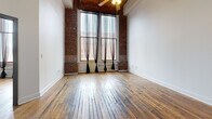 Located at 1000 Washington Ave in downtown St. Louis, this two-bedroom, two-bathroom loft showcases a compelling blend of industrial character and modern updates. Rich, reclaimed hardwood flooring runs throughout the space, complemented by soaring ceilings with exposed ductwork and a warm wood-paneled ceiling accent visible in the hallway. Structural columns and exposed brick walls add authentic loft character, while large floor-to-ceiling windows in the living area flood the space with natural light and offer urban views.

The open-concept kitchen, dining, and living area serves as the heart of the home. The kitchen is outfitted with sage-green cabinetry, dark granite countertops, stainless steel appliances, and a peninsula island — ideal for both cooking and entertaining. A central hallway connects the bedrooms, each featuring hardwood floors and clerestory-style interior windows that allow light to filter through. Bedroom doors with glass pane inserts add a refined industrial touch. Both bathrooms are appointed with granite vanities and matte black fixtures. A dedicated in-unit laundry room with full-size washer and dryer adds everyday convenience, while a utility room and ample closet space ensure practical storage throughout.