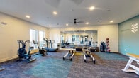 Located in Vestavia Hills, Alabama, this 24-hour fitness room delivers a well-rounded workout environment designed for both cardio training and mind-body exercise. The single-floor space is thoughtfully laid out with distinct functional zones, allowing multiple users to train simultaneously without crowding.

The cardio area is equipped with a treadmill, air bike, rowing machines, and a stair climber, all positioned along a windowed wall that invites ample natural light and exterior views. Ceiling fans overhead provide comfortable airflow throughout the workout.

A dedicated Pilates and strength zone features multiple reformer machines and a Pilates chair, arranged to support guided or independent sessions. A rack of medicine balls and a set of dumbbells round out the free weight offerings. Full-length mirrors are mounted along one wall, extending the sense of space and supporting proper form during exercise.

The room's interior design is both functional and motivating. A teal accent wall displays the encouraging phrase "Keep Going. Keep Growing." alongside decorative botanical motifs, adding a vibrant, uplifting atmosphere. Multi-toned patterned carpet tiles in blue, teal, and gold define the floor space with a modern aesthetic.

Glass-paneled interior doors connect this space to an adjacent fitness area, and recessed lighting throughout ensures consistent illumination at any hour.